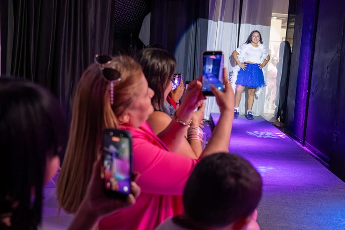Parents photographing a girl in a feather boa and blue skirt as she poses on the catwalk