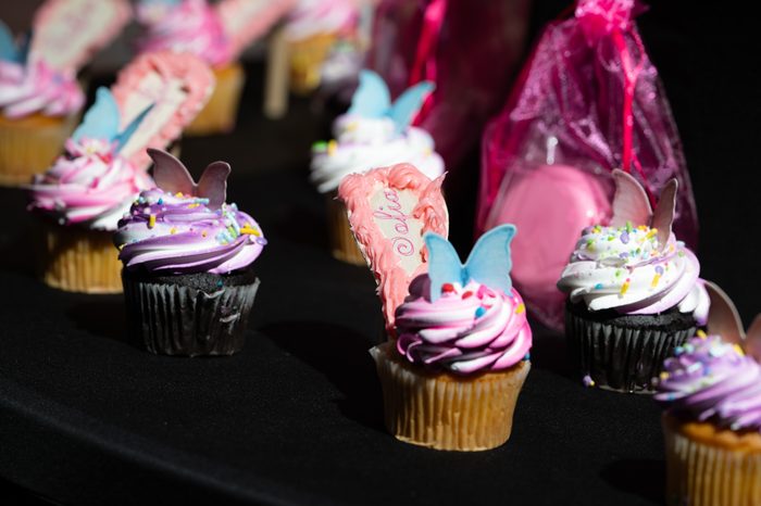 Close-up of butterfly-topped cupcakes with a personalized name topper at the celebration
