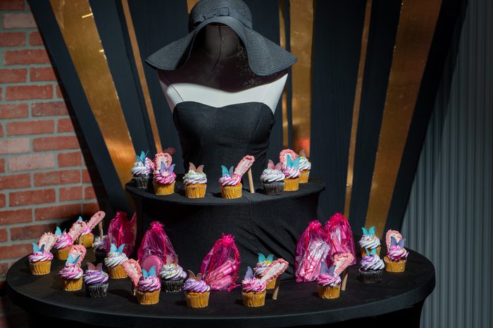 Cupcake tower display with a dressed mannequin, high-heel cupcakes, and gift bags