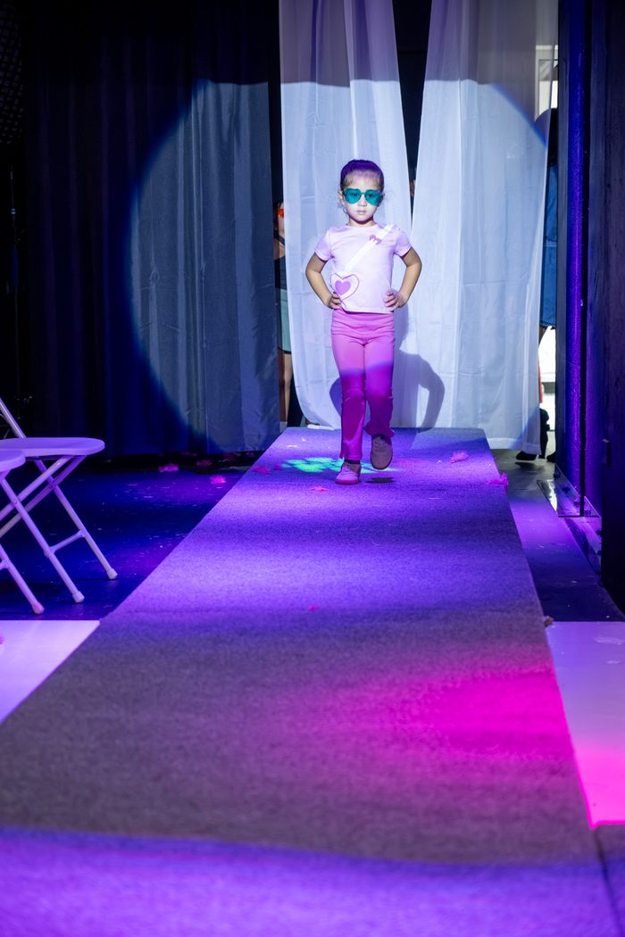Girl in sunglasses practicing her catwalk stride down the illuminated runway
