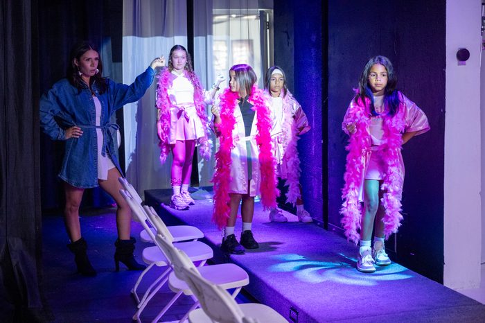 Coach demonstrating a pose to girls in pink boas on the runway